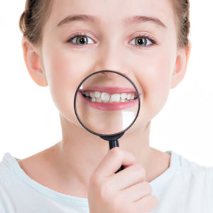 Close-up portrait of cute little girl showing teeth through a magnifying glass - isolated on white.